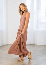 [Color: Clay] A model wearing a timeless cotton blend sleeveless clay brown maxi dress. With a dropped waist, tiered skirt, scooped neckline, and racer back detail.