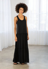 [Color: Black] A model wearing a timeless cotton blend sleeveless black maxi dress. With a dropped waist, tiered skirt, scooped neckline, and racer back detail. 