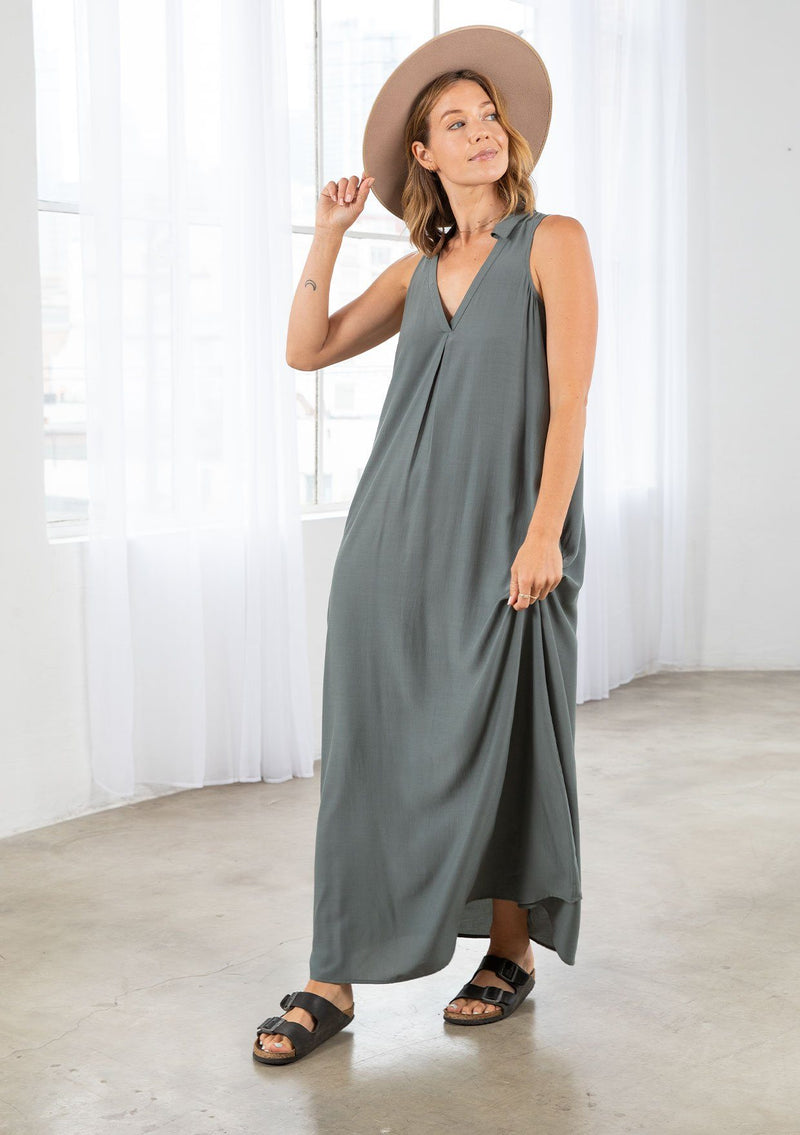 [Color: Moss] A model wearing a moss green, flowy sleeveless maxi dress with a v neckline, a collared neck, and side pockets. 