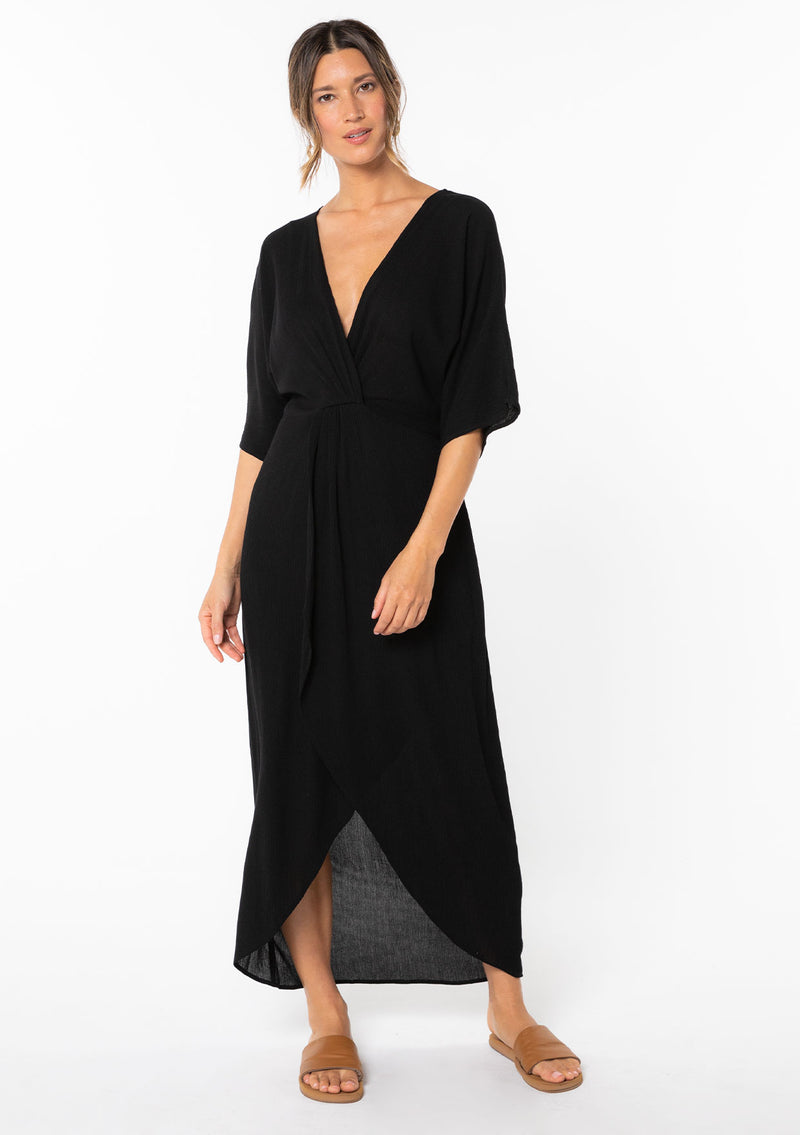 [Color: Black] A model wearing a black maxi dress with a knot front detail and half length kimono sleeves.  
