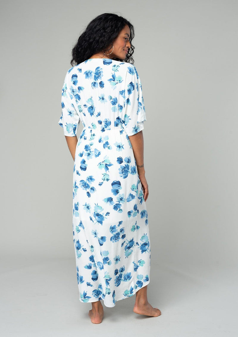 [Color: Ivory/Aqua] A back facing image of a brunette model wearing a classic bohemian resort maxi dress in a white and blue watercolor floral print. With half length kimono sleeves, a twist front waist detail, and a plunging v neckline. 