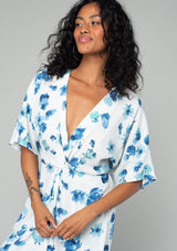 [Color: Ivory/Aqua] A close up front facing image of a brunette model wearing a classic bohemian resort maxi dress in a white and blue watercolor floral print. With half length kimono sleeves, a twist front waist detail, and a plunging v neckline. 