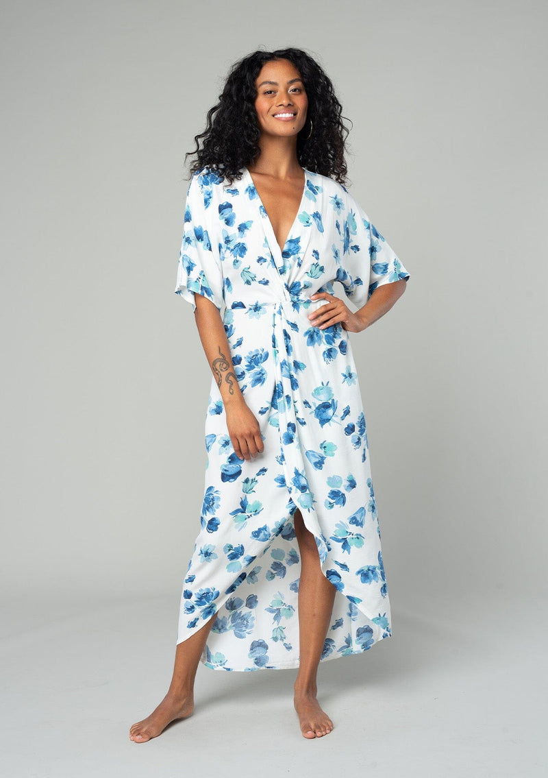 [Color: Ivory/Aqua] A front facing image of a brunette model wearing a classic bohemian resort maxi dress in a white and blue watercolor floral print. With half length kimono sleeves, a twist front waist detail, and a plunging v neckline. 