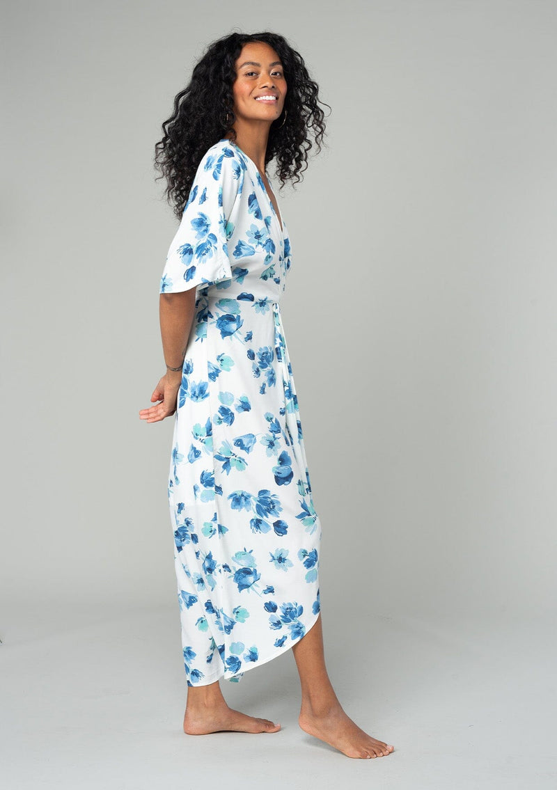 [Color: Ivory/Aqua] A side facing image of a brunette model wearing a classic bohemian resort maxi dress in a white and blue watercolor floral print. With half length kimono sleeves, a twist front waist detail, and a plunging v neckline. 