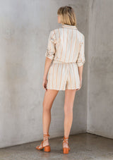 [Color: Natural/Terracotta] A model wearing a linen blend twill short romper in a terracotta yarn dye stripe. With long rolled tab sleeves and a tie waist belt. 