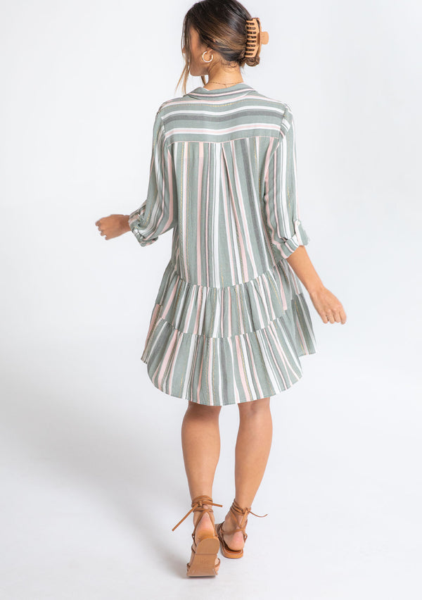 [Color: Olive/Pink] A model wearing an olive green and pink stripe mini shirt dress with long rolled sleeves and a metallic gold thread detail. 