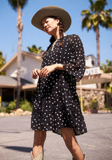 [Color: Black/Ivory] Model wearing a floral embroidered black babydoll mini dress with long voluminous bell sleeves.