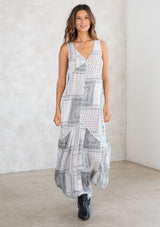 [Color: Off White/Grey] A model wearing a white and grey paisley bandana patchwork print maxi dress. With a self covered button front, a tiered skirt, a v neckline, thicker tank top straps, and a loose flowy fit.