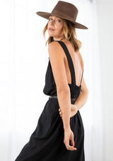 [Color: Black] A model wearing a loose fit mid length dress in a linen blend. With thick tank top straps, a low back, and side pockets.