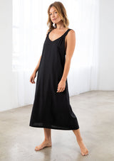 [Color: Black] A model wearing a loose fit mid length dress in a linen blend. With thick tank top straps, a low back, and side pockets.