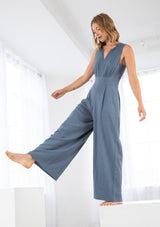 [Color: Denim Blue] A model wearing linen blend full length jumpsuit. With a wide leg, side pockets, a v neckline, and a back zip closure. 