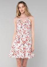 [Color: Natural/Rose] A front facing image of a blonde model wearing a bohemian spring mini dress in a rose pink floral print. With spaghetti straps, a split v neckline with tassel ties, a smocked elastic waist, and a flowy tiered skirt.