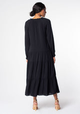 [Color: Black] A model wearing a versatile black bohemian maxi dress. Features a classic peasant dress silhouette, a relaxed fit, and delicate textured dot details throughout.