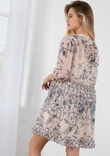 [Color: Light Peach] A blond model wearing a sheer floral print mini dress. Featuring three quarter length sleeves, a button front, and a ruffle trimmed waist.