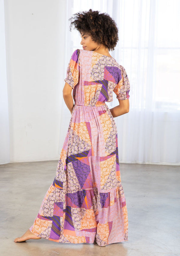 [Color: Pink/Coral] A model wearing a pink and purple floral patchwork print maxi dress. With short puff sleeves, a tiered skirt, and a side slit. 
