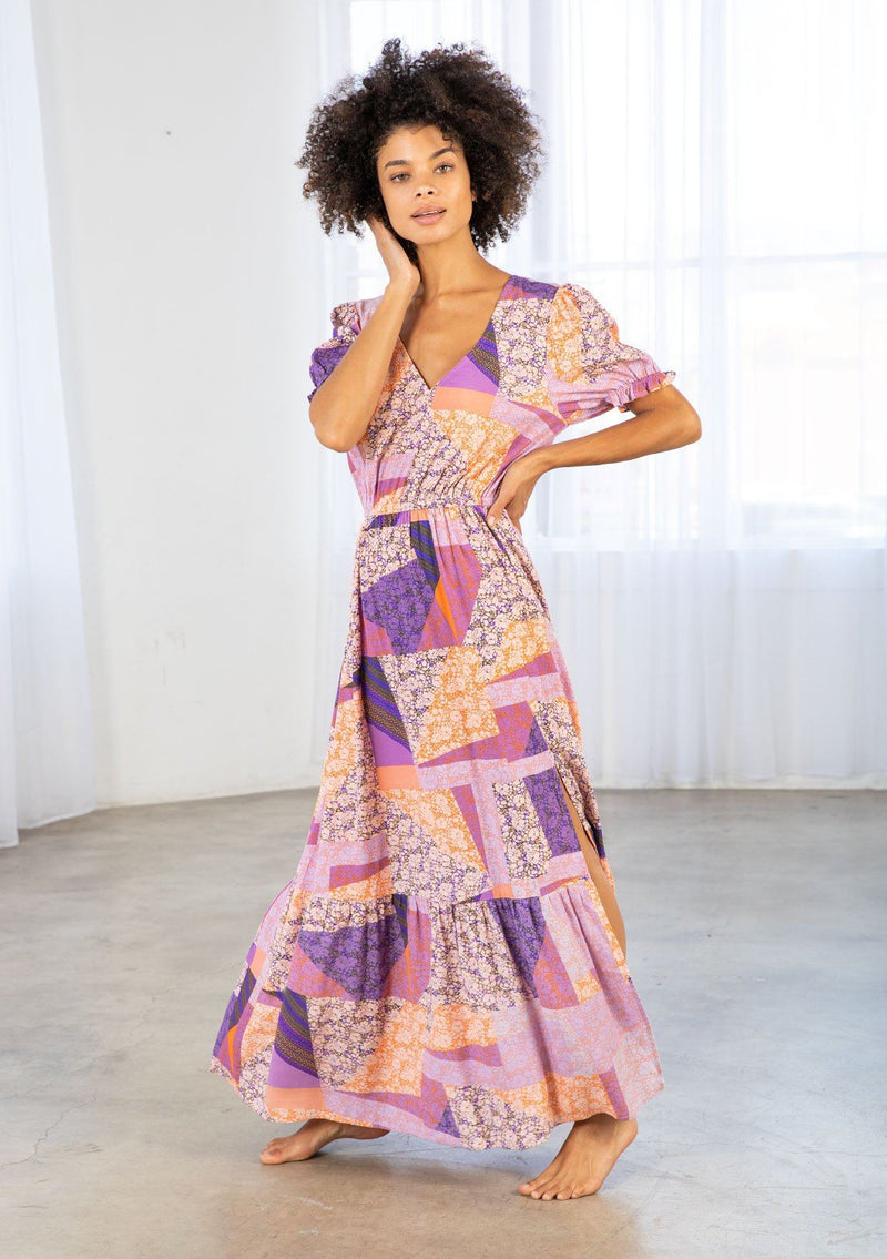 [Color: Pink/Coral] A model wearing a pink and purple floral patchwork print maxi dress. With short puff sleeves, a tiered skirt, and a side slit. 