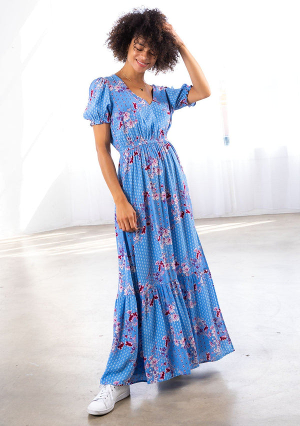 [Color: Azure/Mulberry] A model wearing wearing an ultra feminine azure blue floral print maxi dress. Featuring short puff sleeves and an off center front slit.
