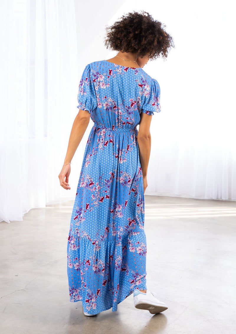 [Color: Azure/Mulberry] A model wearing wearing an ultra feminine azure blue floral print maxi dress. Featuring short puff sleeves and an off center front slit.