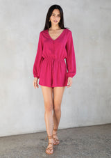 [Color: Mulberry] A model wearing a playful and chic pink short romper in rose jacquard. With long sleeves, a button up front, and a v neckline.