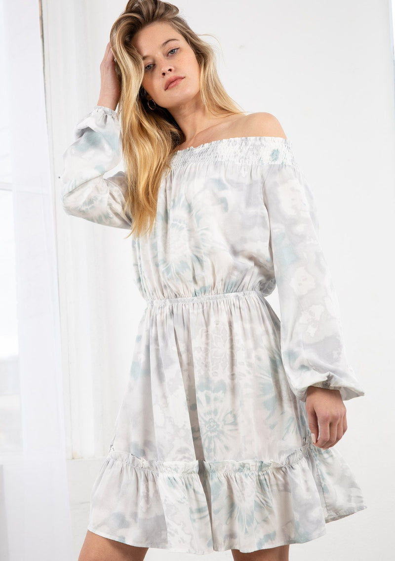 [Color: Lavender/Grey] A blond model wearing a tie dye mini dress. Featuring a smocked off the shoulder detail, an elastic waist, voluminous long sleeves, and a tiered ruffle trimmed skirt. 