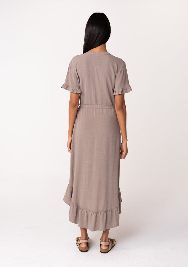 [Color: Latte] A back facing image of a model wearing a beige brown mid length shirt dress in a linen blend. Featuring short sleeves with a ruffled trim, a button up front, an adjustable waist tie, and a ruffled hemline.