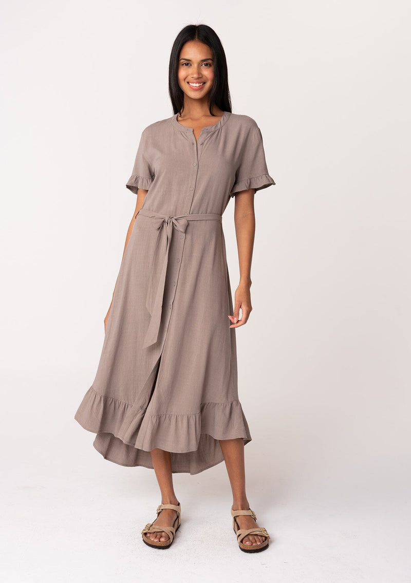 [Color: Latte] A full body front facing image of a model wearing a beige brown mid length shirt dress in a linen blend. Featuring short sleeves with a ruffled trim, a button up front, an adjustable waist tie, and a ruffled hemline.