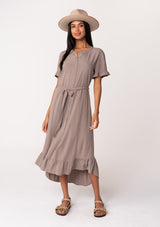 [Color: Latte] A front facing image of a model wearing a beige brown mid length shirt dress in a linen blend. Featuring short sleeves with a ruffled trim, a button up front, an adjustable waist tie, and a ruffled hemline.