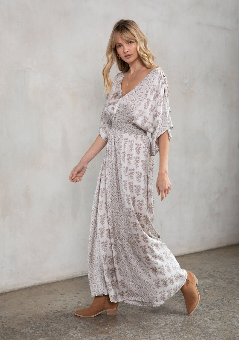 [Color: Natural/Taupe] A model wearing a soft and silky mixed floral print maxi dress. With half length kimono sleeves, a smocked elastic waist, a deep v neckline, and an open back with tassel tie closure.