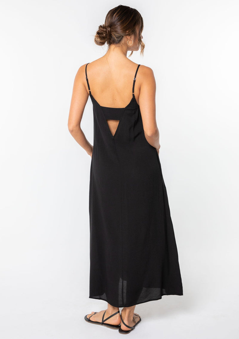 [Color: Black] A model wearing a sleeveless maxi dress. With adjustable spaghetti straps, a ruffle trimmed scooped neckline, and a v back with cutout detail.