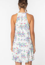 [Color: Ivory/Violet] A model wearing a white sleeveless mini dress with a purple floral print throughout. Featuring a loose and flowy tent silhouette and pleated front. 