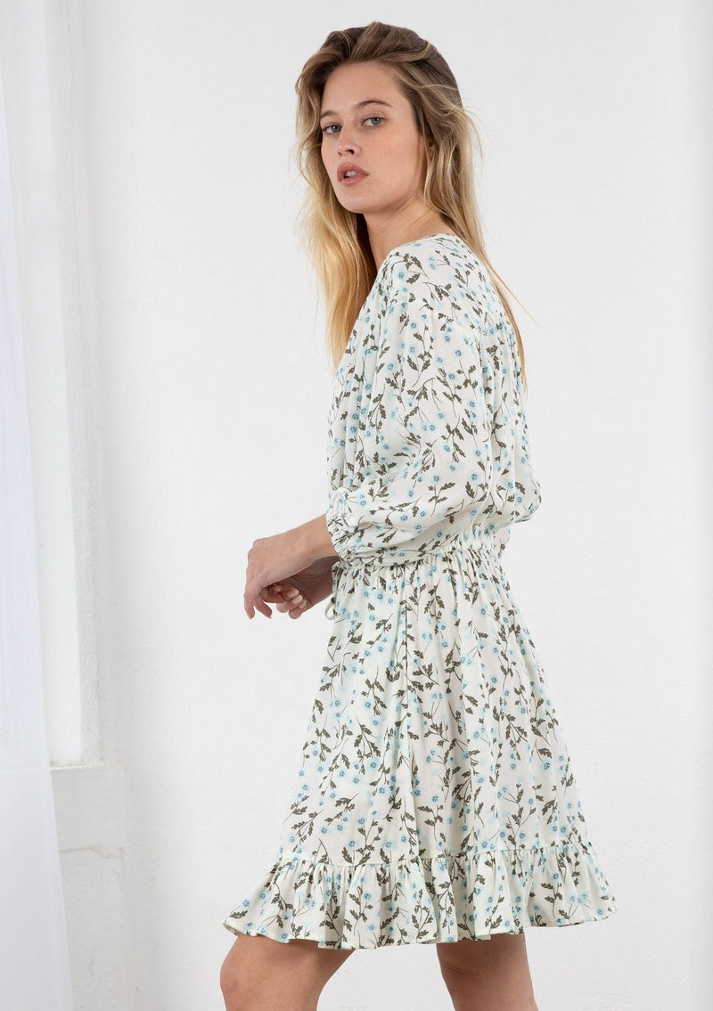 [Color: Ivory/Sky] A blond model wearing a button front mini dress in a small floral print. Featuring long voluminous sleeves, an adjustable tassel tie drawstring waist, and a flounce trimmed skirt. 