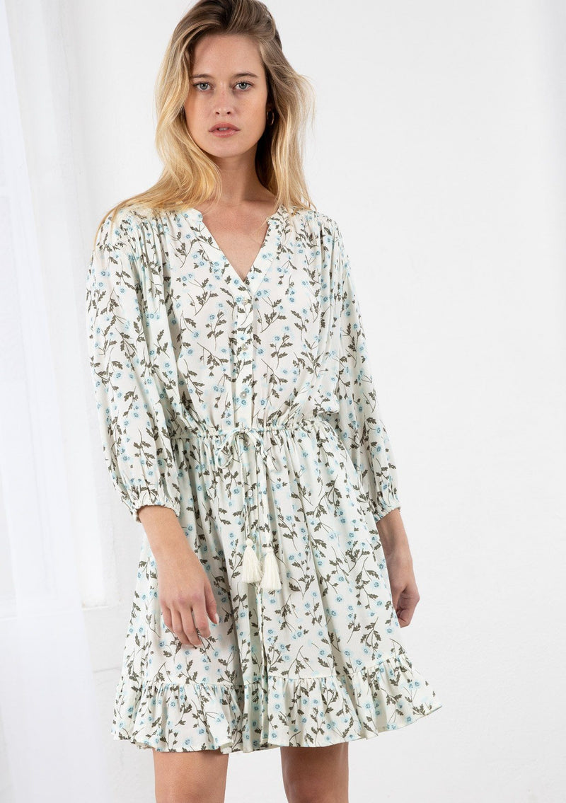 [Color: Ivory/Sky] A blond model wearing a button front mini dress in a small floral print. Featuring long voluminous sleeves, an adjustable tassel tie drawstring waist, and a flounce trimmed skirt. 