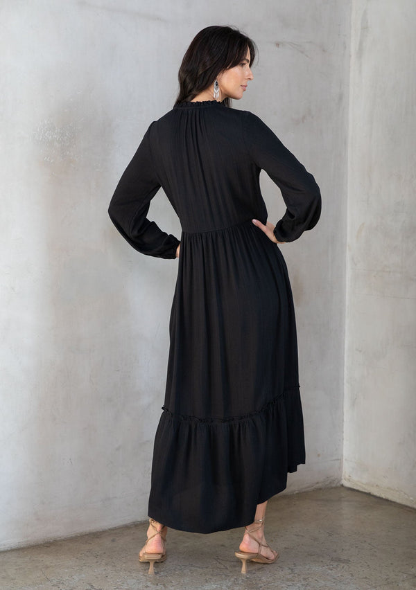 [Color: Black] A model wearing a flowy black bohemian maxi dress with long sleeves and a button front. 