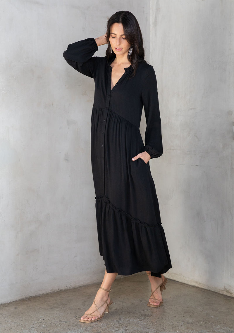[Color: Black] A model wearing a flowy black bohemian maxi dress with long sleeves and a button front. 