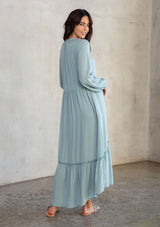 [Color: Dusty Teal] A model wearing a timeless light teal maxi peasant dress with a button front, ruffled neckline, long voluminous sleeves, and tiered skirt. 