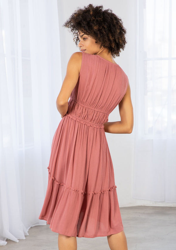 [Color: Terracotta] A model wearing a pink gauze sleeveless mini dress. With embroidered eyelet detail along the waist and shoulder, and elastic waist, and a tiered high low skirt. 