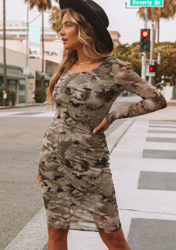 [Color: Olive/Coffee] A model wearing a micro mesh mini dress in a camouflage print. With long sleeves, a round neckline, and a slim bodycon fit.