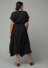 [Color: Black] A back facing image of a brunette model wearing a black cotton button front maxi dress with short sleeves and an allover textured gingham.