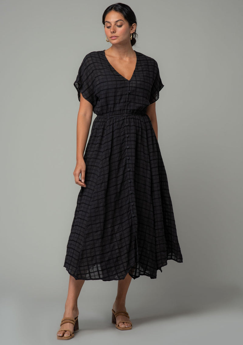 [Color: Black] A full body front facing image of a brunette model wearing a black cotton button front maxi dress with short sleeves and an allover textured gingham.