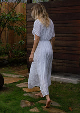 [Color: White] A full body back facing image of a blonde woman standing outside with wearing a white cotton button front maxi dress with short sleeves and an allover textured gingham.