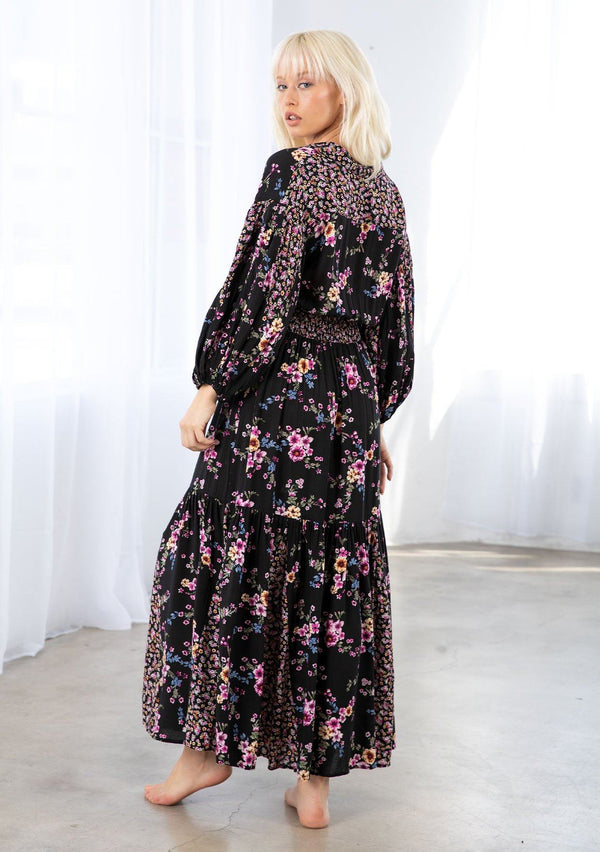 [Color: Black/Wine] A model wearing a flowy bohemian button front maxi dress in a mixed floral print. With three quarter length voluminous sleeves, a collared neckline, a smocked elastic waist, and a contrast floral print paneled skirt. 