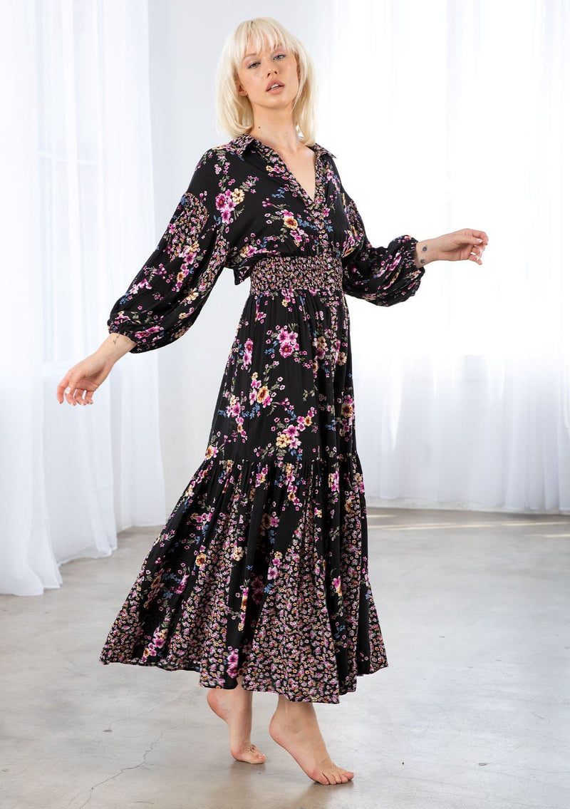 [Color: Black/Wine] A model wearing a flowy bohemian button front maxi dress in a mixed floral print. With three quarter length voluminous sleeves, a collared neckline, a smocked elastic waist, and a contrast floral print paneled skirt. 