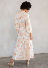 [Color: Natural/Peach] A model wearing a flowy bohemian button front maxi dress in an off white and peach floral print. With three quarter length voluminous sleeves, a collared neckline, a smocked elastic waist, and a contrast floral print paneled skirt.