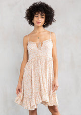 [Color: Natural/Peach] A model wearing a flirty mini dress in an off white and peach ditsy floral print. With a strappy adjustable back, ruffle trimmed neckline with keyhole detail, and a loose flowing fit.