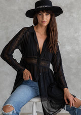 [Color: Black] A model wearing a sheer black mini dress. With lace trimmed long sleeves, a button front, a collared neckline, and a lace trimmed waist. Removable slip included. 