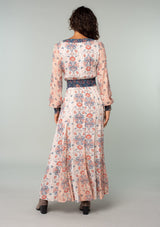 [Color: Ivory/Coral] A back facing image of a brunette model wearing an ivory white, coral pink, and blue mixed floral print bohemian maxi dress. With long sleeves, a v neckline, a smocked elastic waist, and a paneled flowy skirt. 