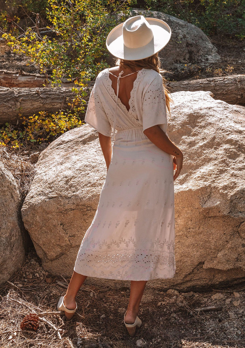 [Color: Bone] A model wearing a cream bohemian embroidered eyelet maxi dress with half length kimono sleeves, a surplice v neckline in front and back, and open back with tie detail, and a long flowy skirt.