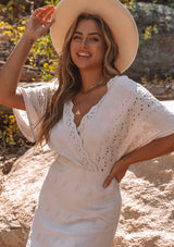 [Color: Bone] A model wearing a cream bohemian embroidered eyelet maxi dress with half length kimono sleeves, a surplice v neckline in front and back, and open back with tie detail, and a long flowy skirt.