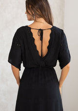 [Color: Black] A model wearing a black bohemian embroidered eyelet maxi dress with half length kimono sleeves, a surplice v neckline in front and back, and open back with tie detail, and a long flowy skirt. 