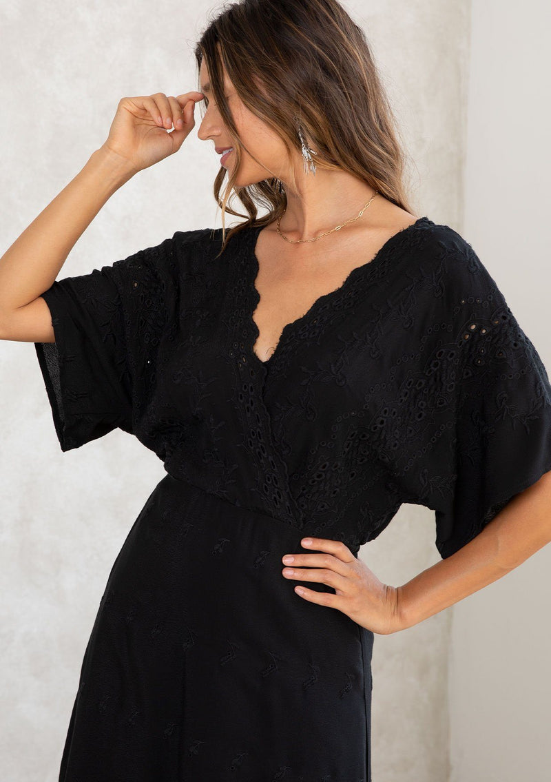 [Color: Black] A model wearing a black bohemian embroidered eyelet maxi dress with half length kimono sleeves, a surplice v neckline in front and back, and open back with tie detail, and a long flowy skirt. 